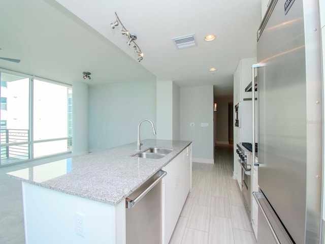 kitchen featuring white cabinetry, an island with sink, light stone countertops, stainless steel appliances, and sink