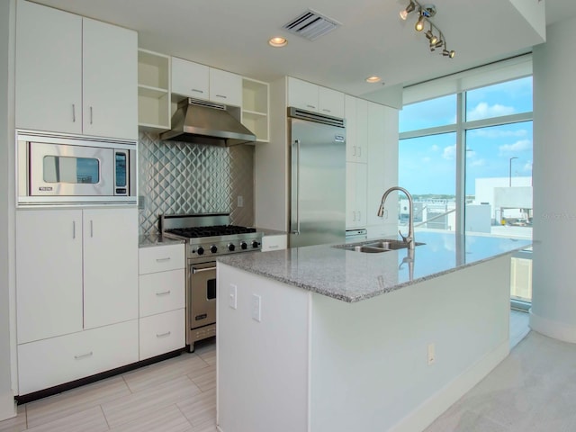 kitchen with a kitchen island with sink, white cabinets, built in appliances, and sink