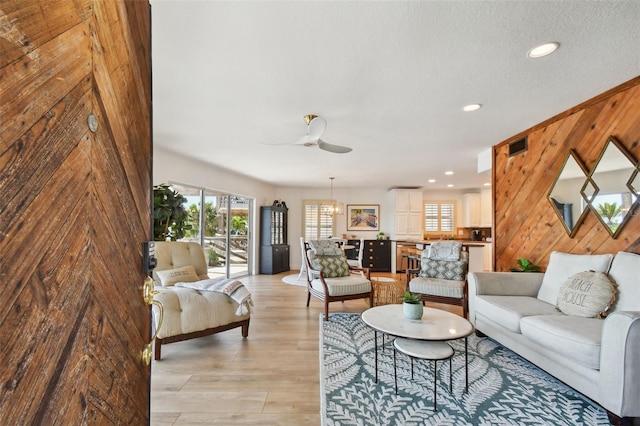 living room with ceiling fan, wooden walls, light wood-type flooring, and a textured ceiling