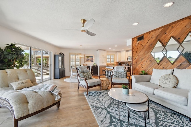 living room with a textured ceiling, wood walls, ceiling fan, and light hardwood / wood-style flooring