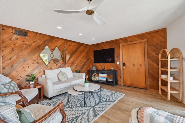 living room featuring light wood-type flooring, a textured ceiling, wooden walls, and ceiling fan