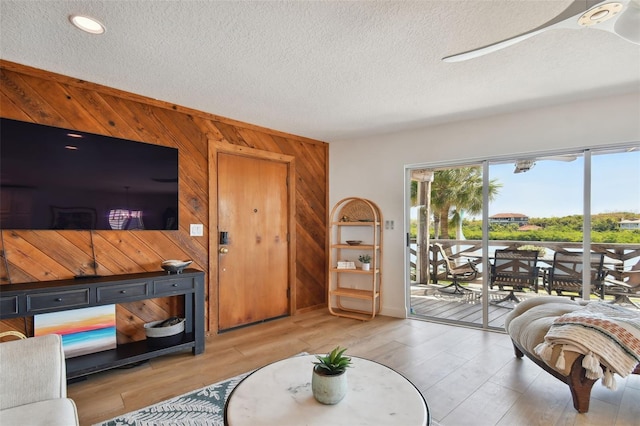 living room featuring ceiling fan, a textured ceiling, wood walls, and light hardwood / wood-style floors