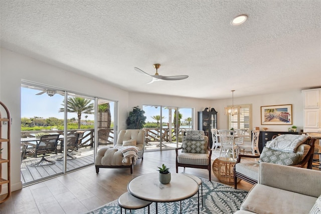 living room featuring a textured ceiling, ceiling fan with notable chandelier, and light hardwood / wood-style floors