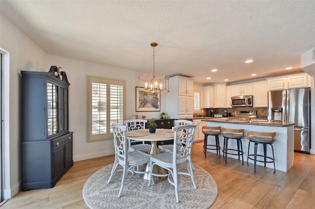 dining space featuring light wood-type flooring, a chandelier, and a textured ceiling