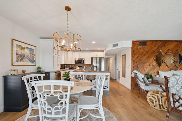 dining space with wooden walls, light wood-type flooring, a notable chandelier, and a textured ceiling