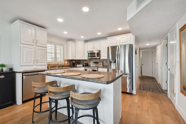 kitchen featuring light wood-type flooring, stainless steel appliances, a center island, and white cabinetry