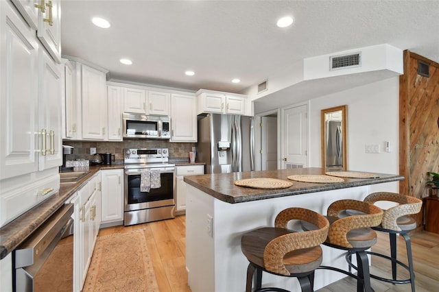 kitchen featuring light wood-type flooring, a breakfast bar area, white cabinetry, backsplash, and appliances with stainless steel finishes