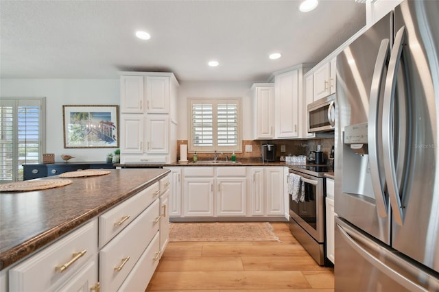 kitchen with sink, white cabinetry, stainless steel appliances, light hardwood / wood-style floors, and decorative backsplash