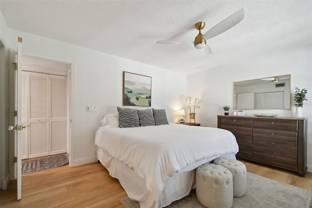 bedroom with a textured ceiling, light hardwood / wood-style floors, ceiling fan, and a closet