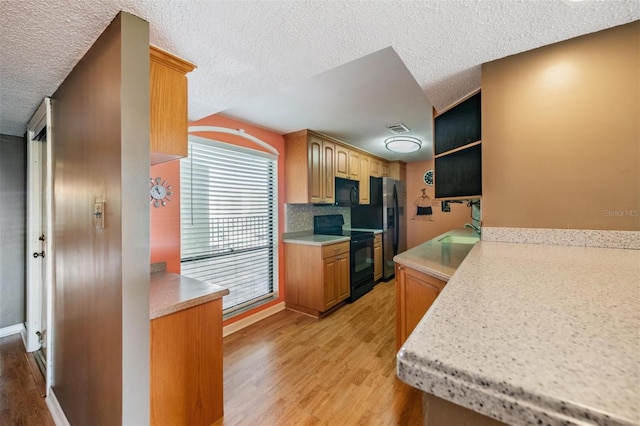 kitchen with a textured ceiling, light wood-type flooring, stainless steel fridge, and electric range