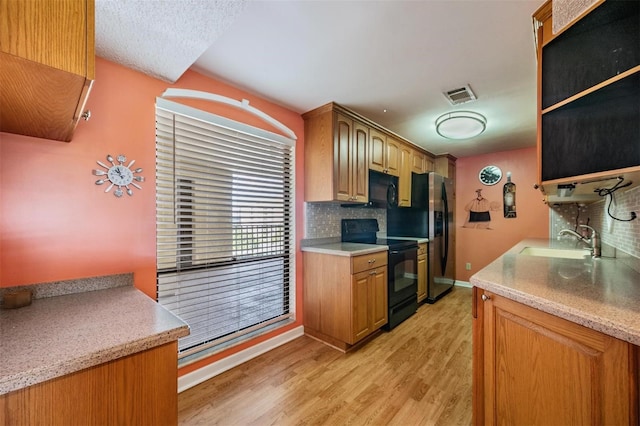 kitchen featuring light wood-type flooring, black appliances, sink, and tasteful backsplash