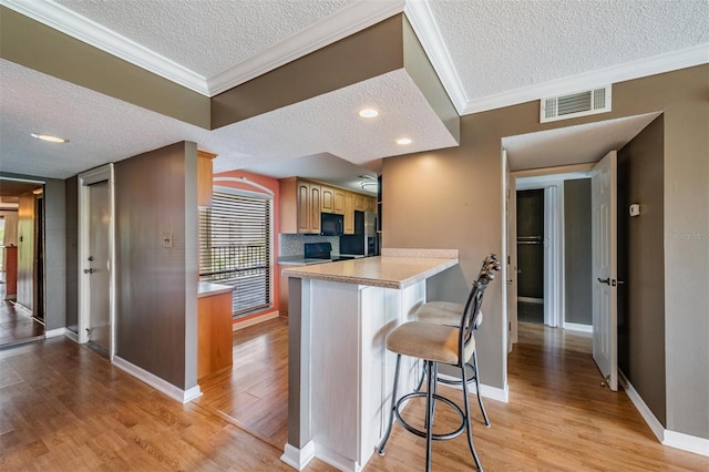 kitchen featuring light wood-type flooring, a textured ceiling, a kitchen breakfast bar, and crown molding