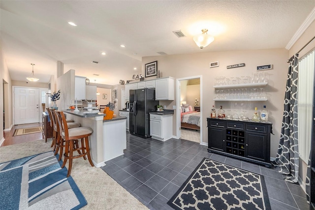 kitchen with lofted ceiling, a breakfast bar area, kitchen peninsula, black fridge with ice dispenser, and white cabinets