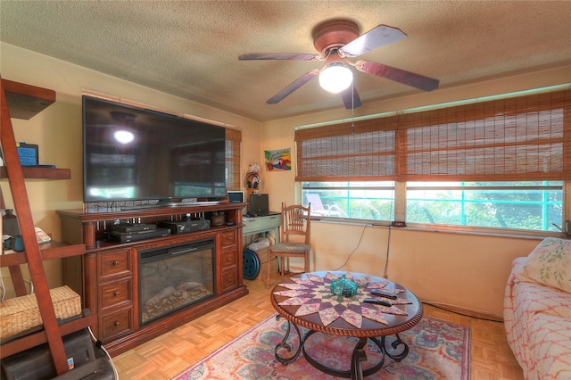 living area with a glass covered fireplace, a healthy amount of sunlight, ceiling fan, and a textured ceiling