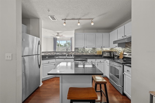 kitchen featuring ceiling fan, white cabinetry, stainless steel appliances, a center island, and a breakfast bar area