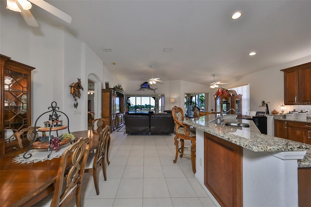 kitchen with light stone countertops, vaulted ceiling, light tile patterned floors, a breakfast bar area, and sink