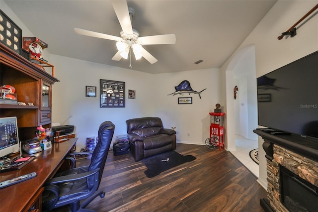 home office featuring ceiling fan, a stone fireplace, and dark hardwood / wood-style floors