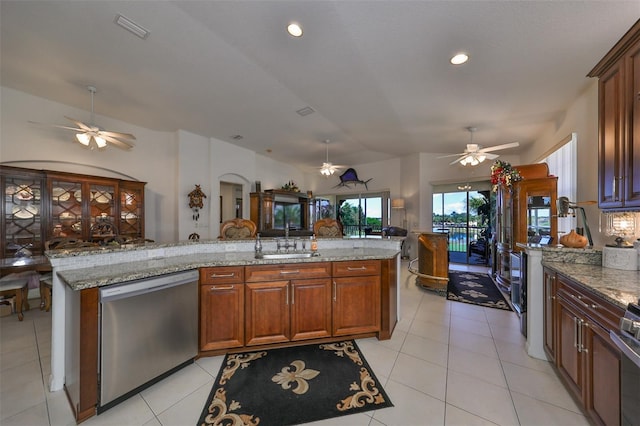 kitchen with light stone countertops, stainless steel dishwasher, light tile patterned floors, a kitchen island with sink, and sink