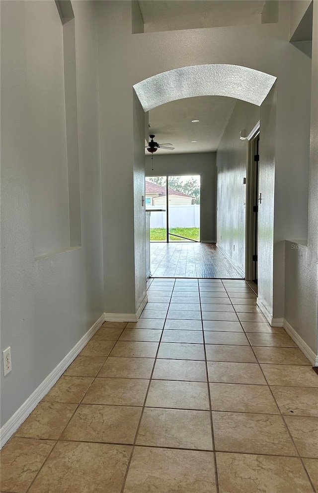 hall with light tile patterned floors, baseboards, and arched walkways