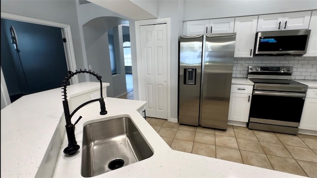 kitchen featuring tasteful backsplash, light countertops, appliances with stainless steel finishes, white cabinetry, and a sink