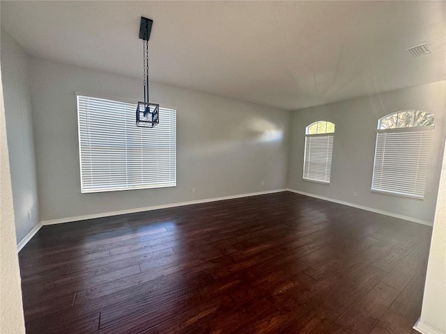 unfurnished room featuring dark wood-style flooring, visible vents, and baseboards