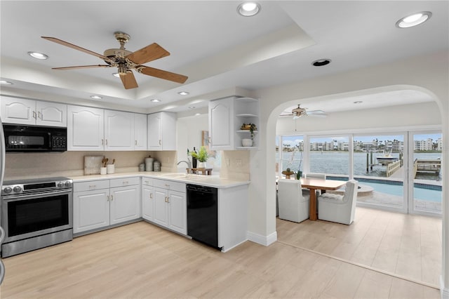 kitchen featuring black appliances, ceiling fan, a sink, a tray ceiling, and white cabinetry