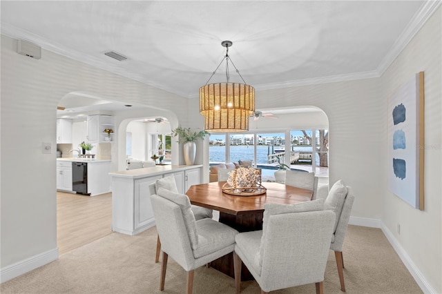 dining room featuring a water view, light carpet, crown molding, and ceiling fan