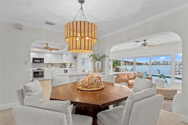 dining space featuring ceiling fan, light carpet, a water view, and ornamental molding