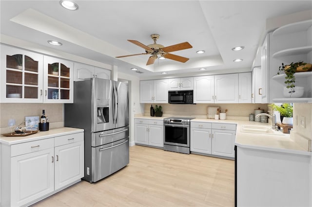 kitchen with stainless steel appliances, a tray ceiling, a sink, open shelves, and decorative backsplash