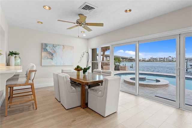 dining area with ceiling fan, a water view, and light hardwood / wood-style flooring