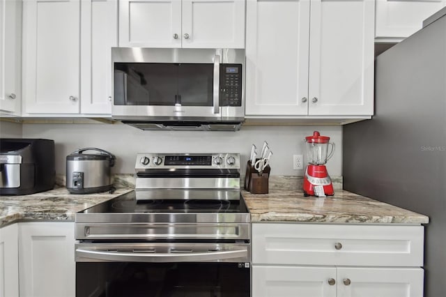 kitchen with appliances with stainless steel finishes, light stone counters, and white cabinets