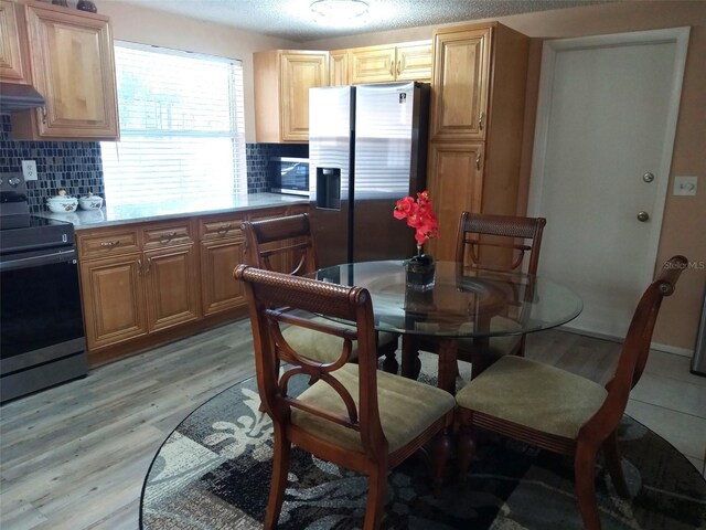 kitchen with light brown cabinets, tasteful backsplash, light hardwood / wood-style floors, a textured ceiling, and appliances with stainless steel finishes