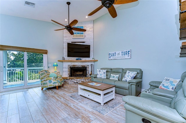 living room with ceiling fan, a fireplace, high vaulted ceiling, and light wood-type flooring