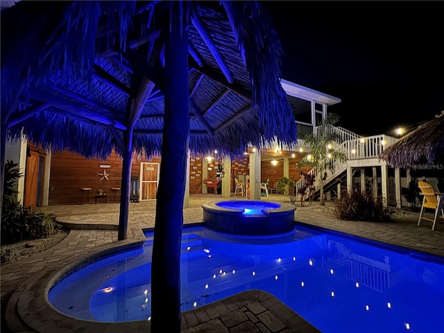 pool at twilight with an in ground hot tub and a patio