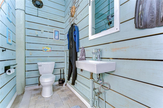 bathroom featuring wooden walls, sink, and toilet