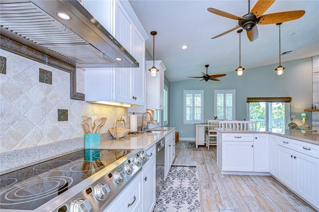 kitchen with lofted ceiling, white cabinetry, wall chimney range hood, and a wealth of natural light