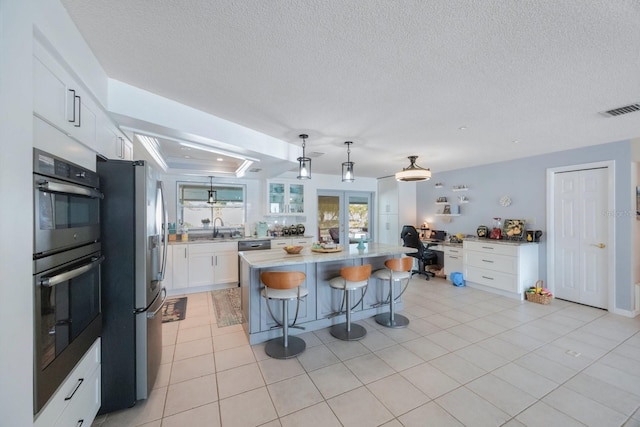 kitchen with white cabinets, a kitchen island, appliances with stainless steel finishes, a breakfast bar, and pendant lighting