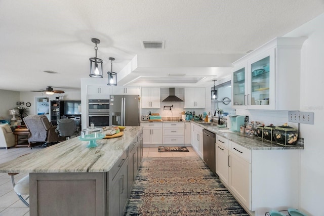 kitchen featuring white cabinetry, light stone counters, stainless steel appliances, and wall chimney range hood