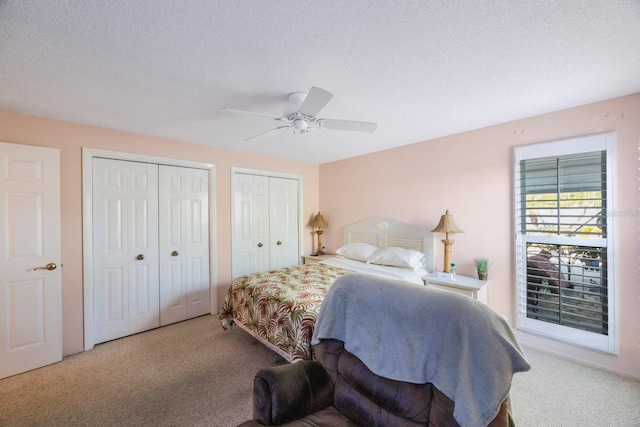 carpeted bedroom with a textured ceiling, multiple closets, and ceiling fan