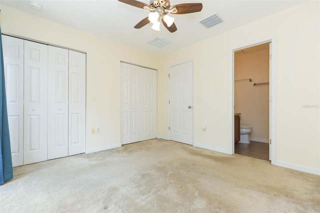 unfurnished bedroom with connected bathroom, two closets, light carpet, and ceiling fan