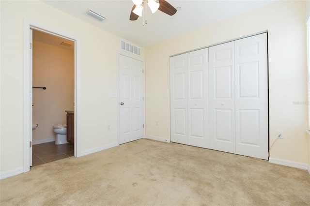 unfurnished bedroom with ensuite bath, ceiling fan, light colored carpet, and a closet