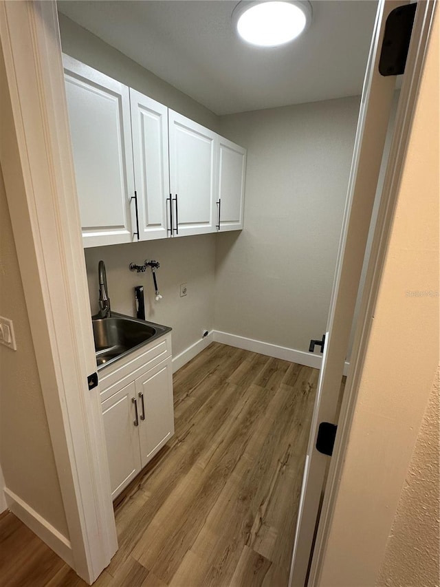 laundry area with washer hookup, sink, light hardwood / wood-style flooring, and cabinets