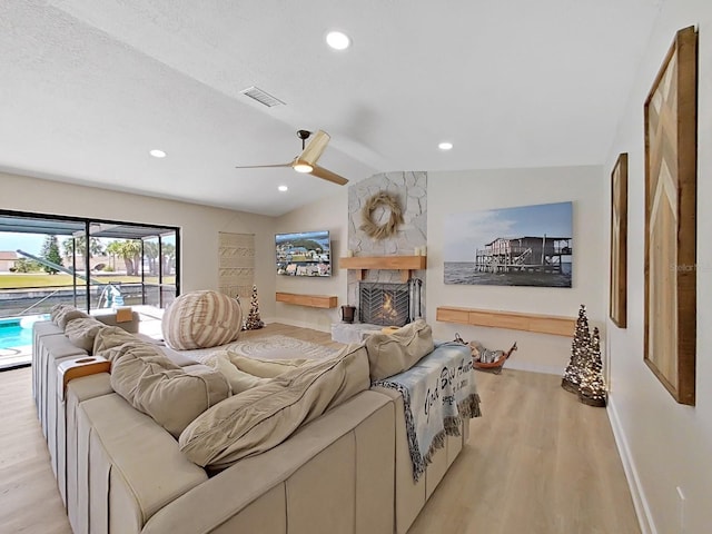 living room with lofted ceiling, light hardwood / wood-style flooring, ceiling fan, a fireplace, and a textured ceiling