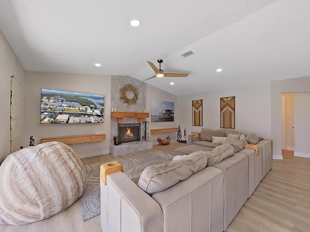 living room featuring ceiling fan, a fireplace, vaulted ceiling, and light hardwood / wood-style flooring