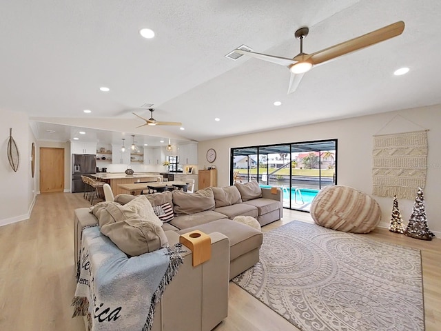 living room with vaulted ceiling, a textured ceiling, ceiling fan, and light hardwood / wood-style flooring