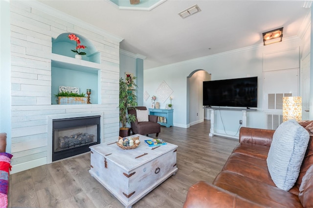 living room featuring wood-type flooring, crown molding, and a large fireplace