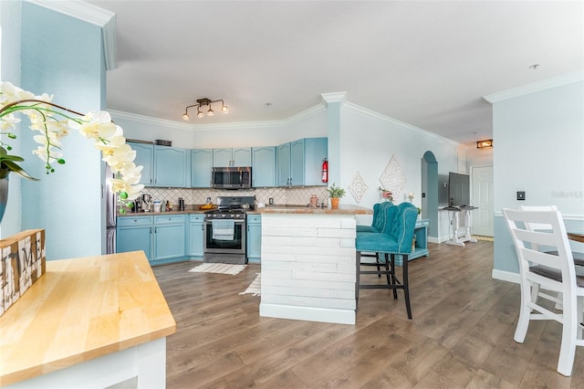 kitchen with appliances with stainless steel finishes, kitchen peninsula, blue cabinetry, wooden counters, and dark hardwood / wood-style floors