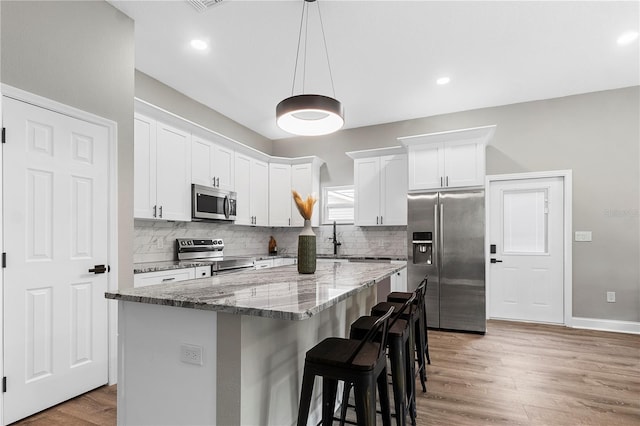 kitchen featuring light wood-type flooring, a center island, white cabinets, decorative backsplash, and stainless steel appliances