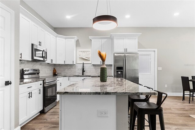 kitchen with hanging light fixtures, a kitchen island, light hardwood / wood-style flooring, white cabinetry, and stainless steel appliances