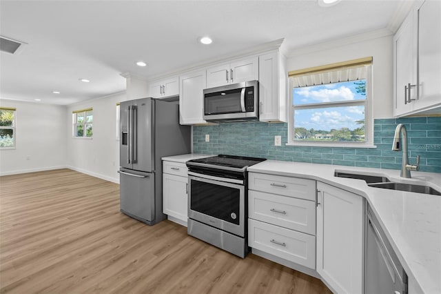 kitchen with crown molding, appliances with stainless steel finishes, sink, white cabinets, and light hardwood / wood-style flooring